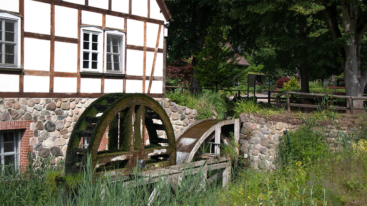 Staré mlýnské kolo Boltenmühle u 53.0372067, 12.8039617 v oblasti Ruppiner Schweiz před historickou hrázděnou budovou.